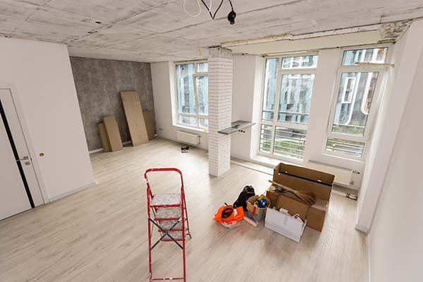 Leerer Raum mit großen Fenstern während der Renovierung, mit Leiter und Kartons